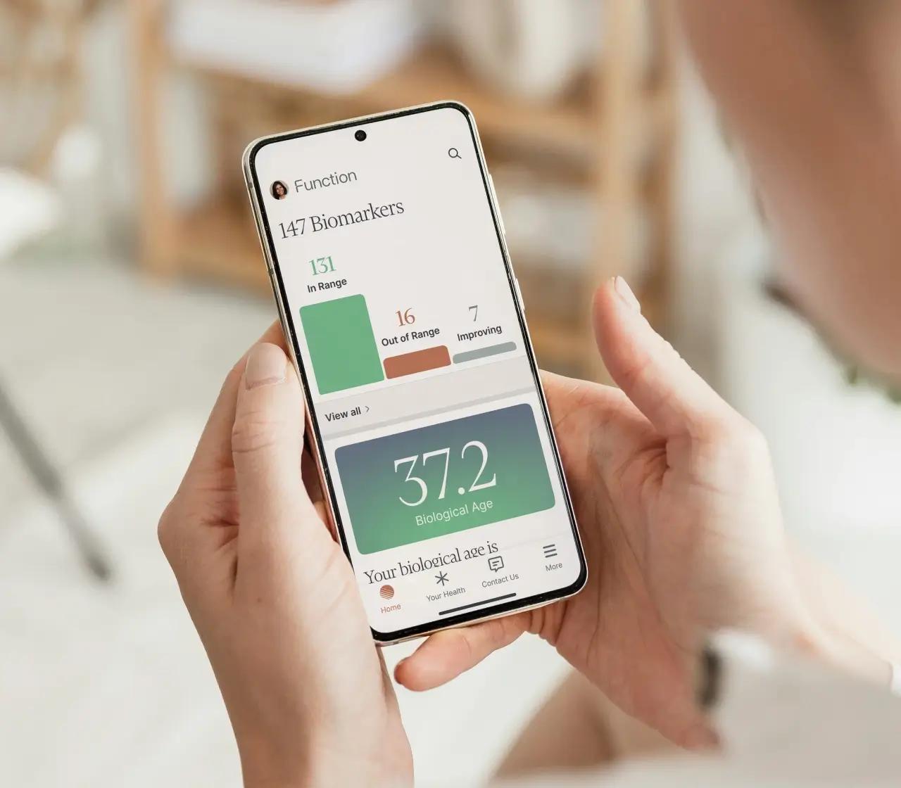 Person holding phone showcasing Function Health results with 100+ biomarkers and a biological age of 37.2.