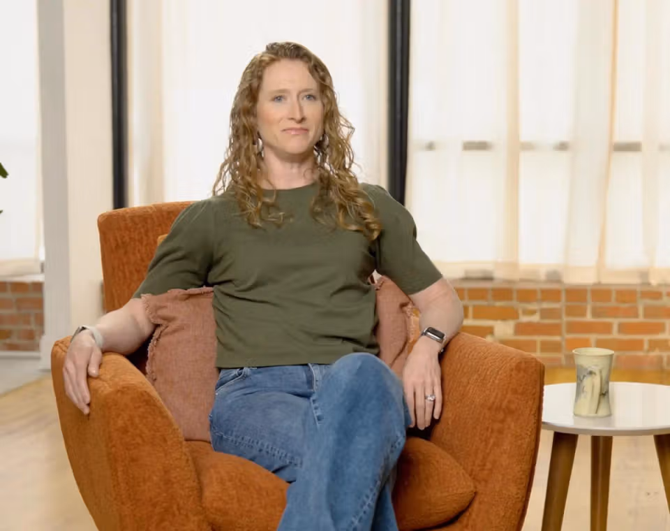 Emeline seated in an orange chair in a bright room, facing the camera.