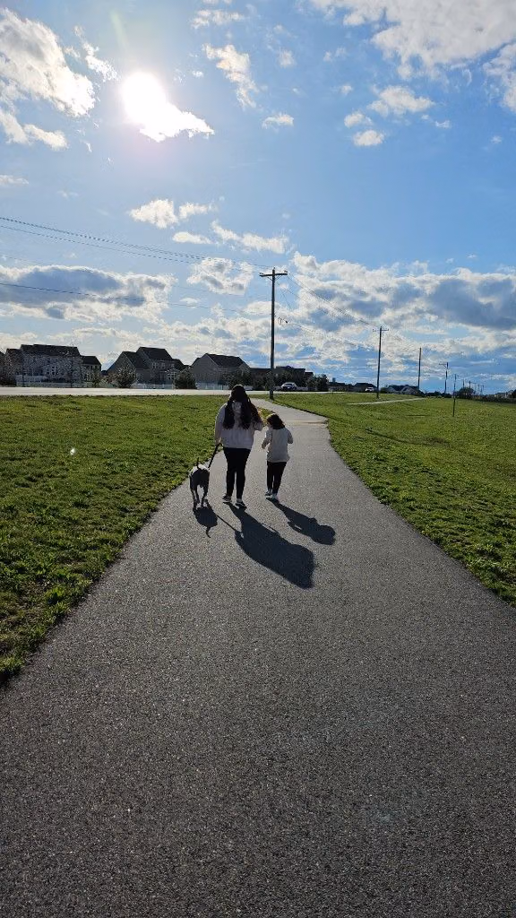 Sarah walking outdoors on a paved path with her daughter and dog.