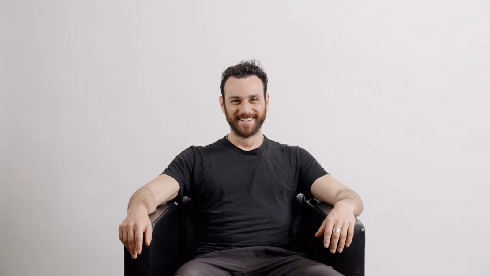 Zack seated in a chair wearing a black T-shirt and smiling at the camera.