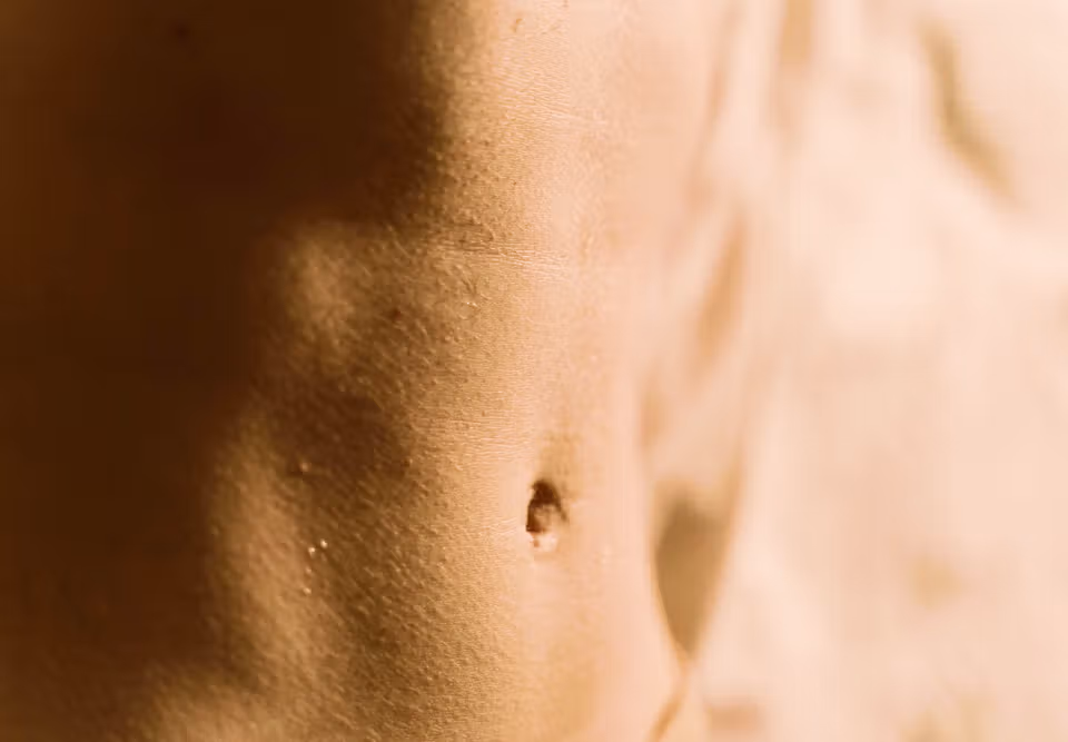 Person sitting on a bed with hands on their abdomen in the colorectal cancer symptoms explainer.