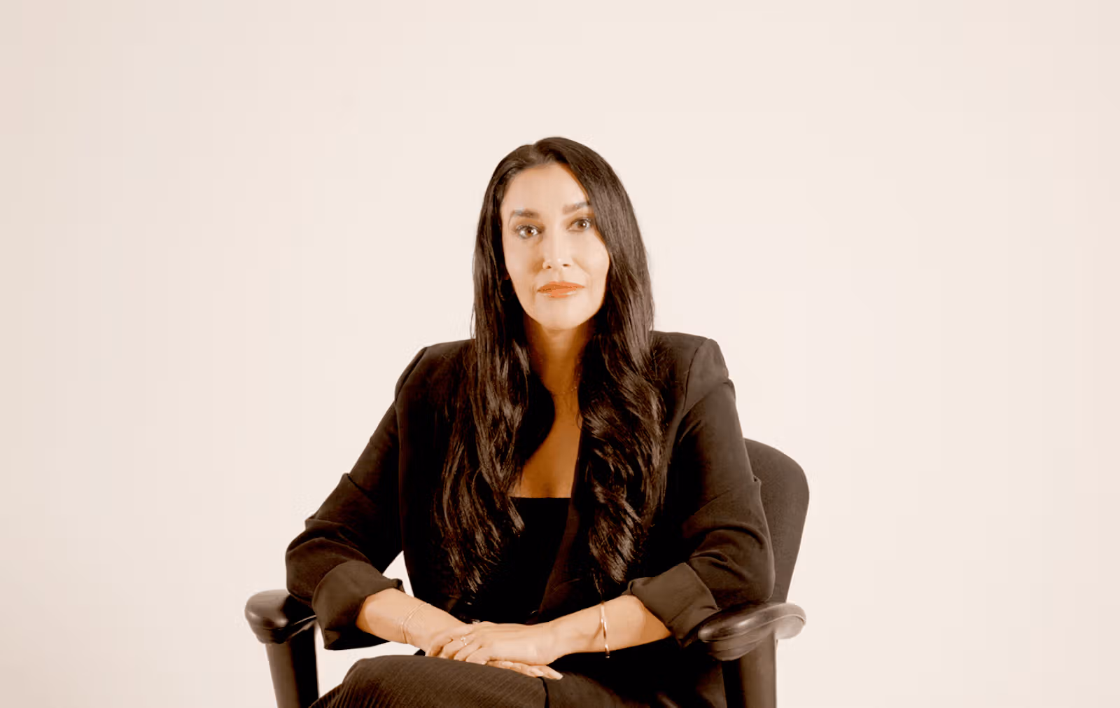 Rebecca seated in a black blazer against a light studio backdrop.
